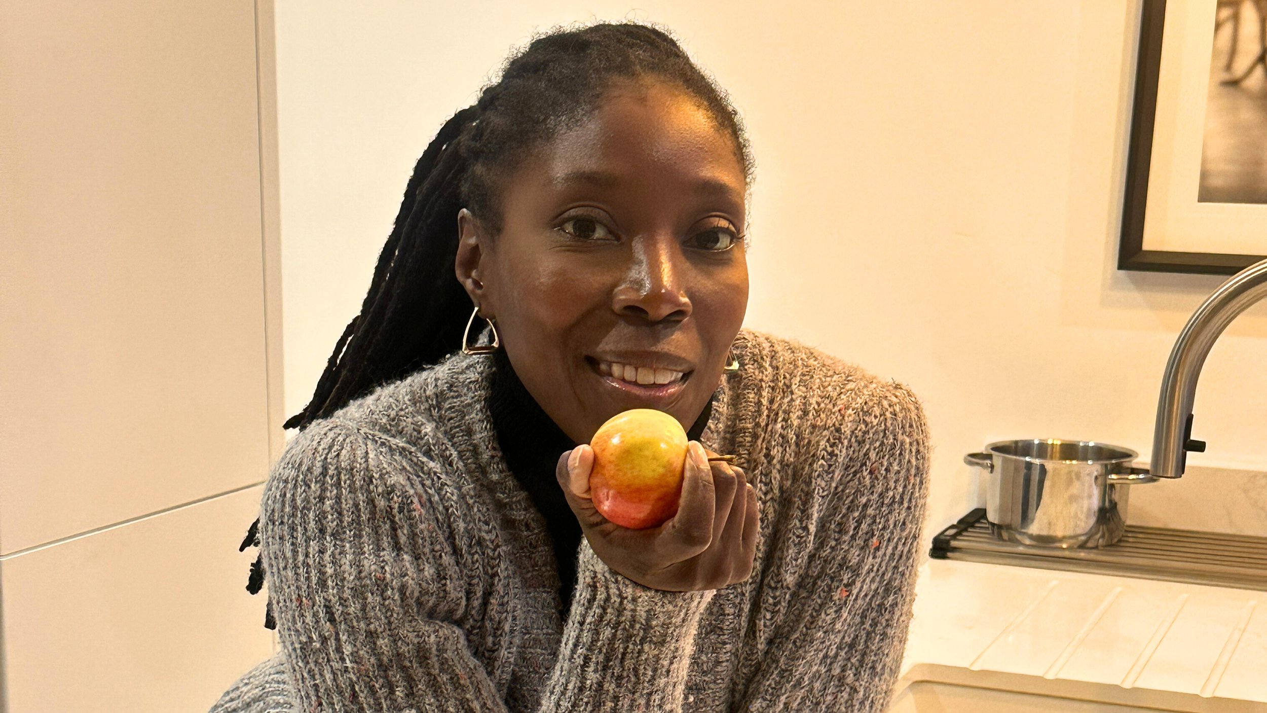 Woman holding a yellow and red apple in a kitchen.