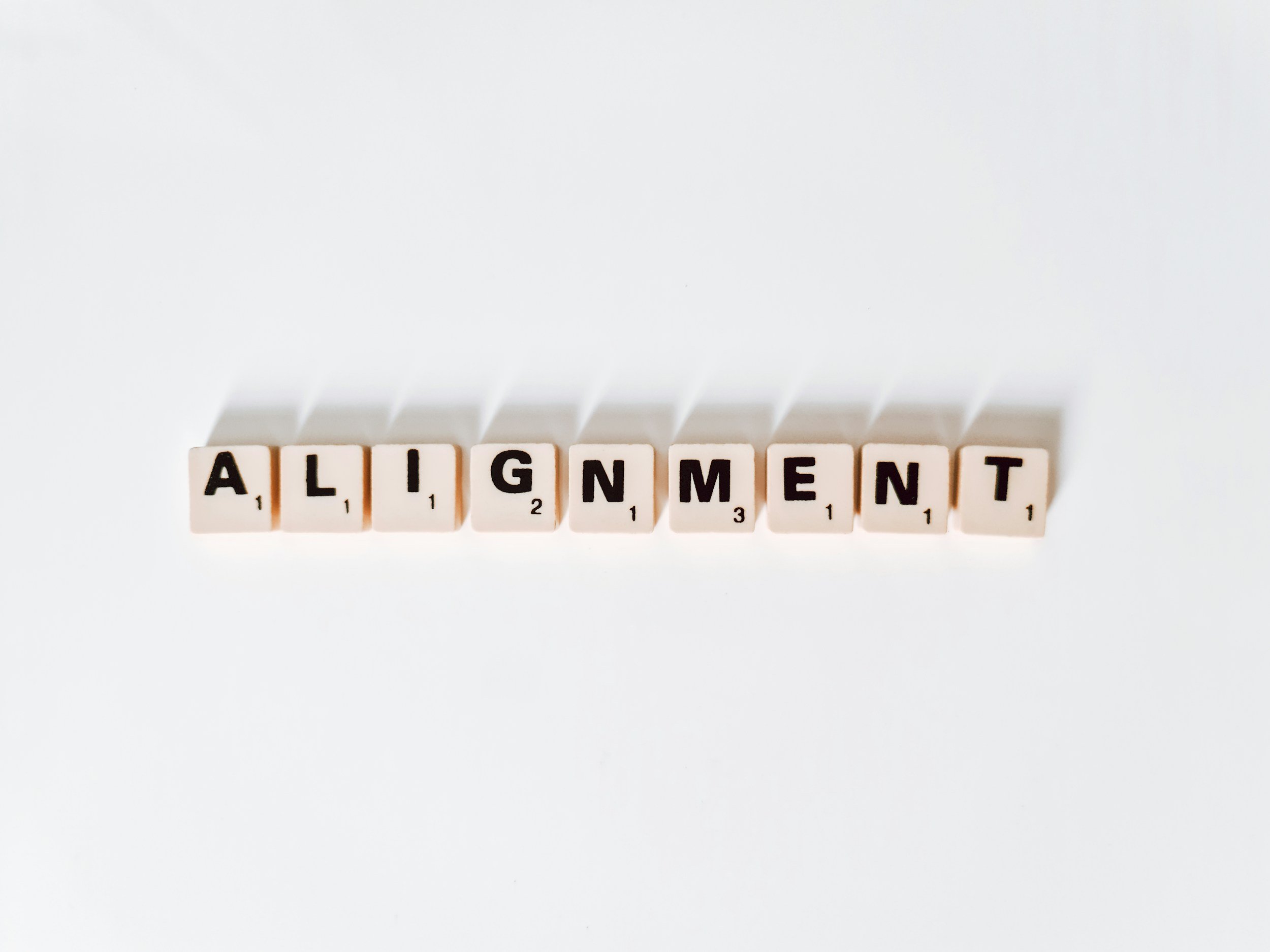Scrabble tiles spelling out the word 'ALIGNMENT' on a white surface.